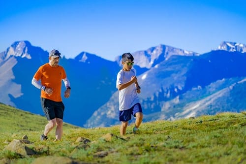 Father and young son jogging on a green hill with mountain range in background