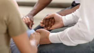 Several people sitting in a prayer circle. Close up of their hands holding each other.