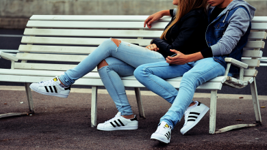 Young couple sitting outside on a bench, dressed similarly with blue jeans and matching sneakers.