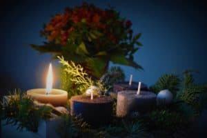 A Christmas candle burns brightly near a branch and other candles