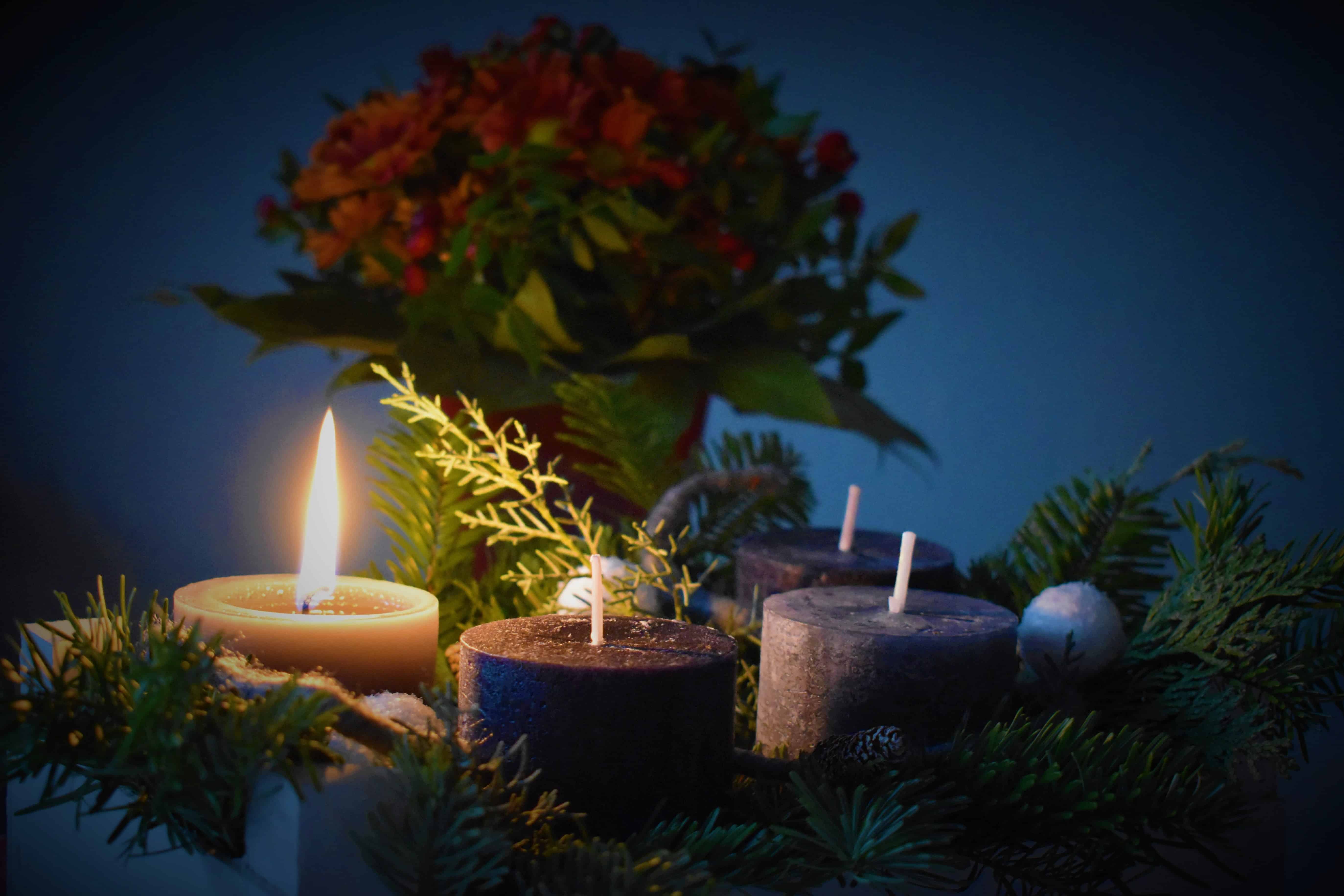A Christmas candle burns brightly near a branch and other candles