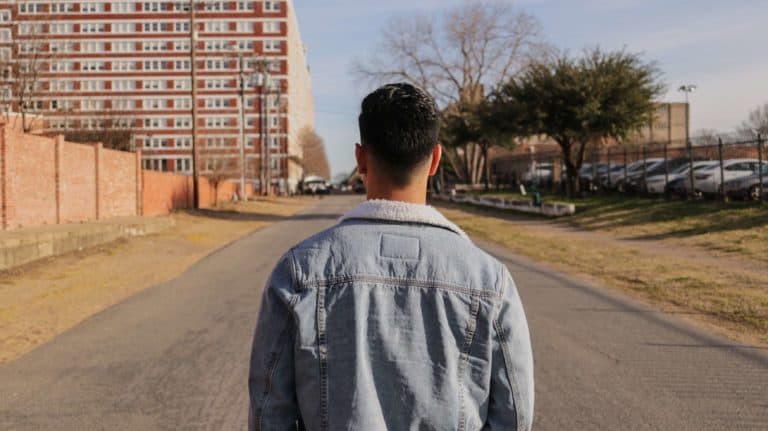 Shown from behind, a young man looking down the middle of an empty town street