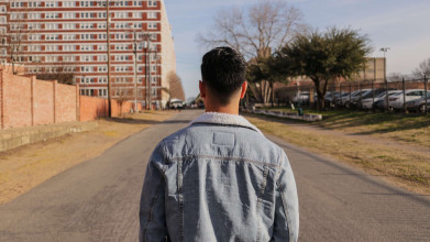 Shown from behind, a young man looking down the middle of an empty town street