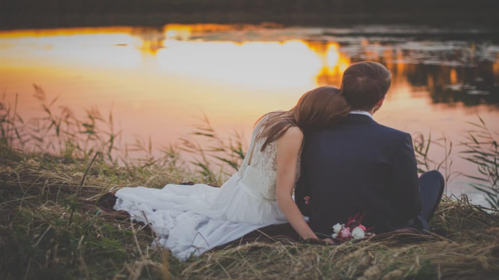 a newly married couple gazes on a pond at sunset