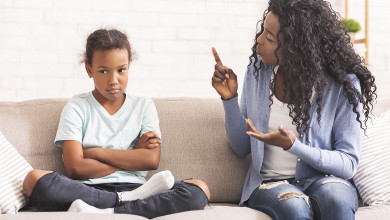 Mother and tween daughter sitting on a couch. Mom is trying to talk to the annoyed girl who’s looking away.