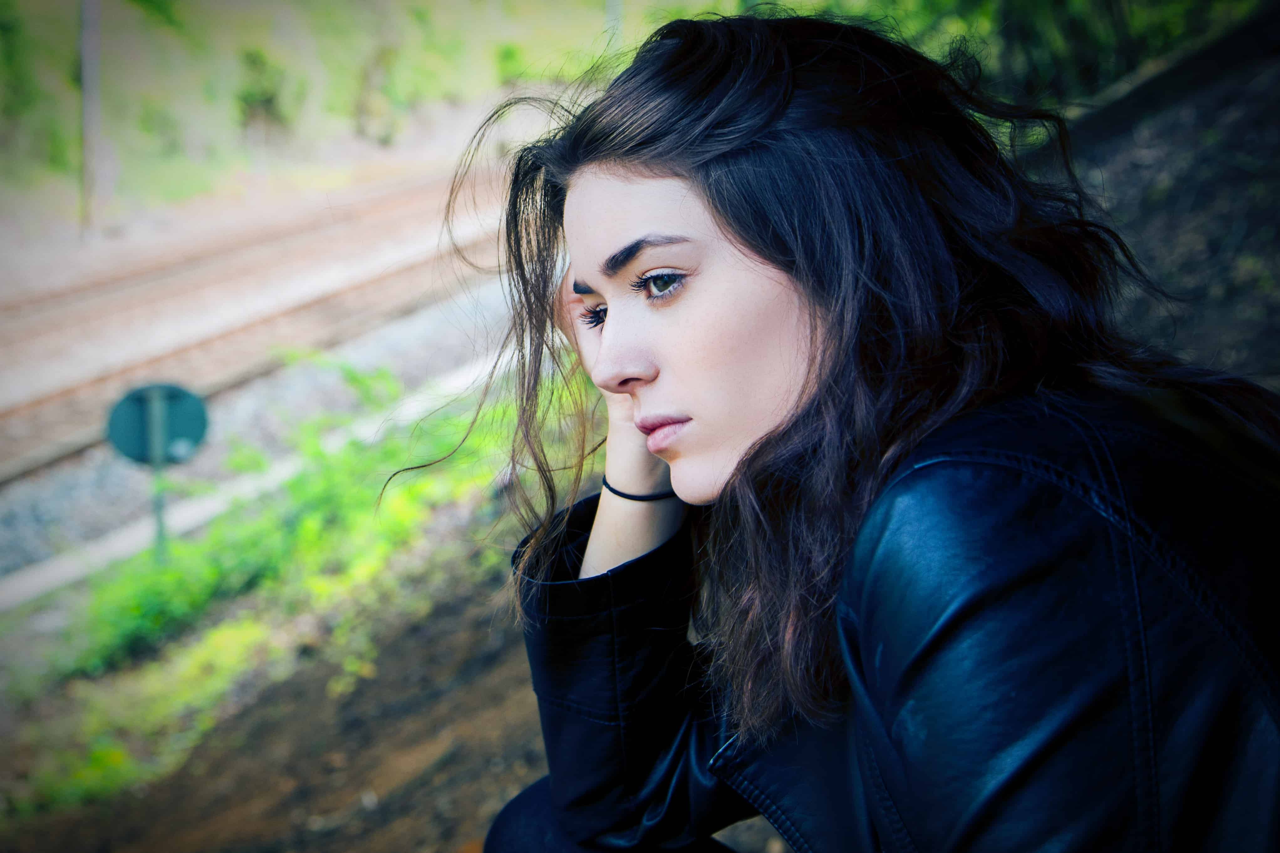 Serious-looking dark-haired woman leaning her head on her hand, looking into the distance