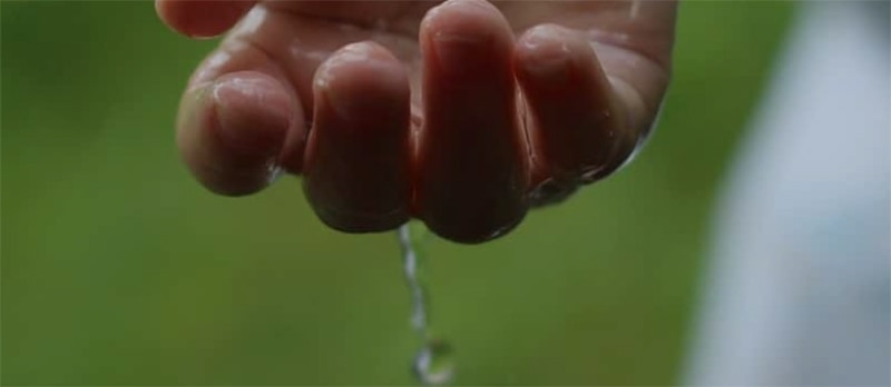 Close up of a girl's or woman's wet hand with water dripping through her fingers against a green background