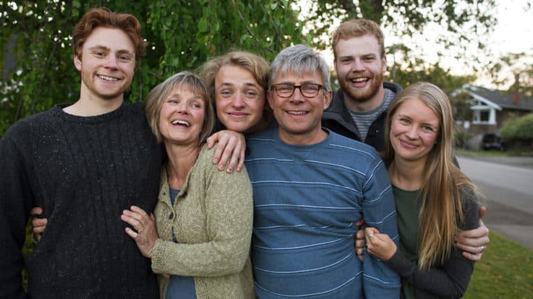 Boomer parents snuggled up with older kids. They are connected and fun loving looking at the camera.