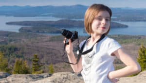Girl holding up a camera with mountainous lakes in the background