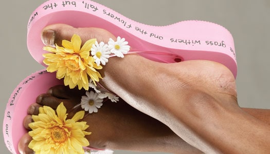Close up of black woman's feet wearing pink flip flops with flowers and writing on the sides