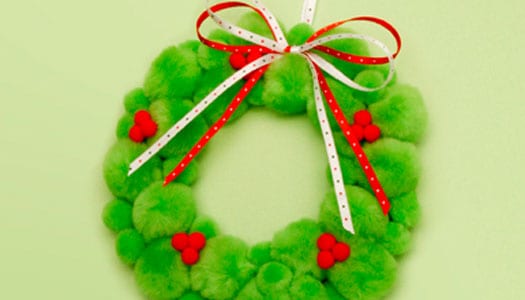 Christmas wreath made out of puffy green fuzzy balls with small groups of red balls and a bow at the top