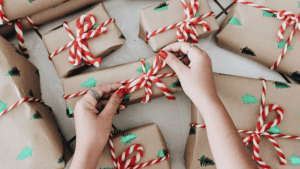 Close up of a woman's hands tying a bow on one of several small Christmas packages