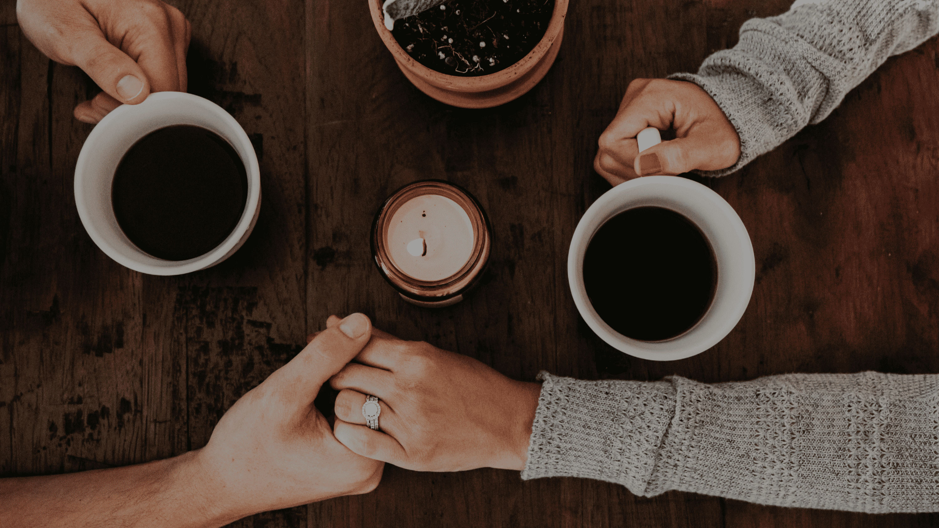 A man and woman hold hands and share coffee