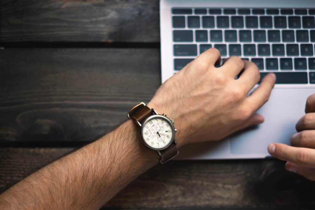 a man looks at his watch while looking at a computer