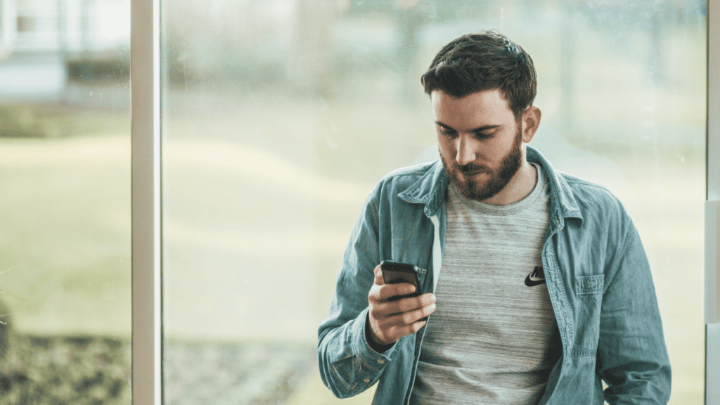 A man standing in front of a sliding glass door looking at his cell phone