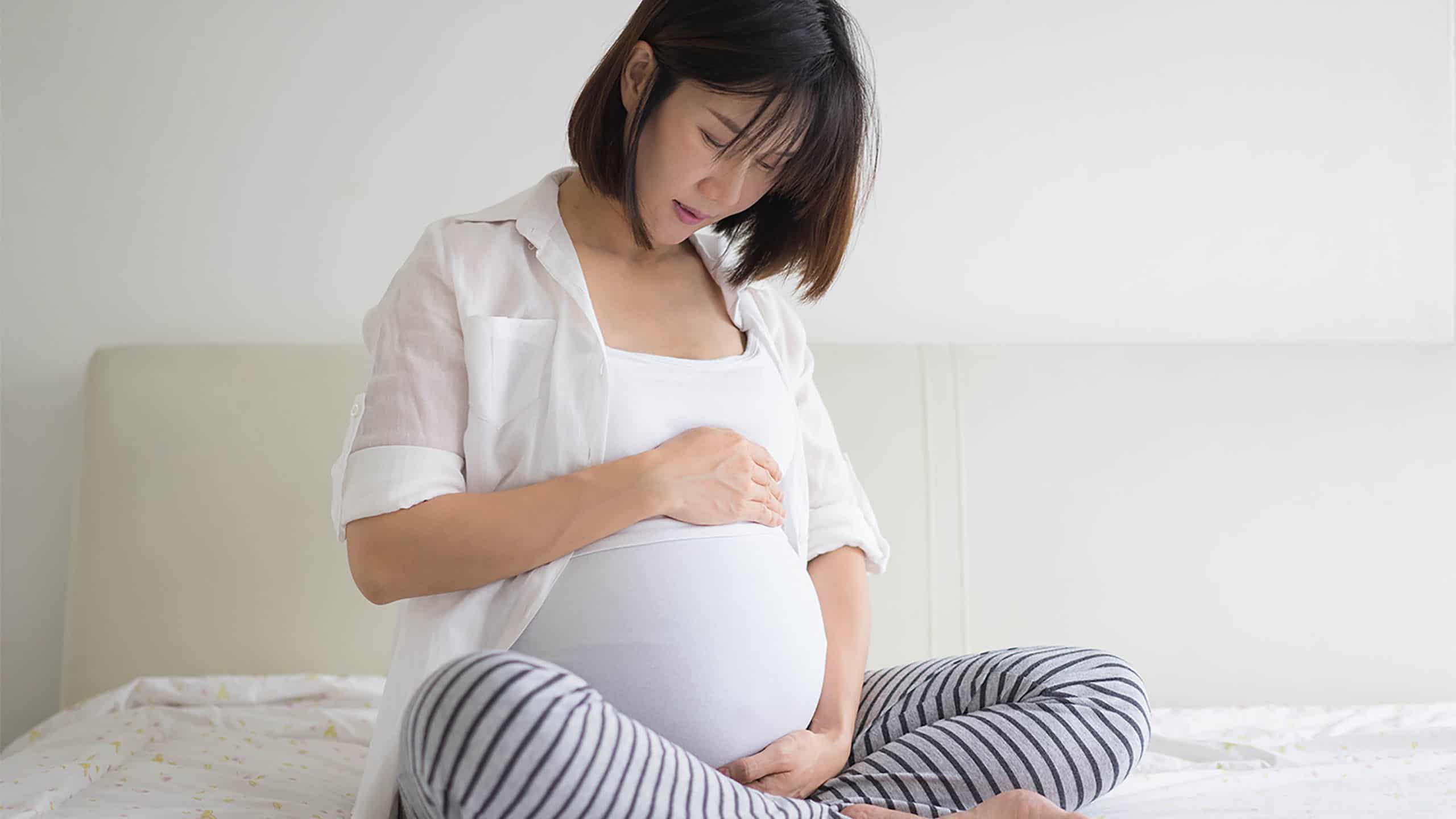 Pregnant woman sitting on her bed and touching her belly with care