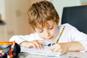 Homeschooling little boy sitting at a table writing with a pencil.