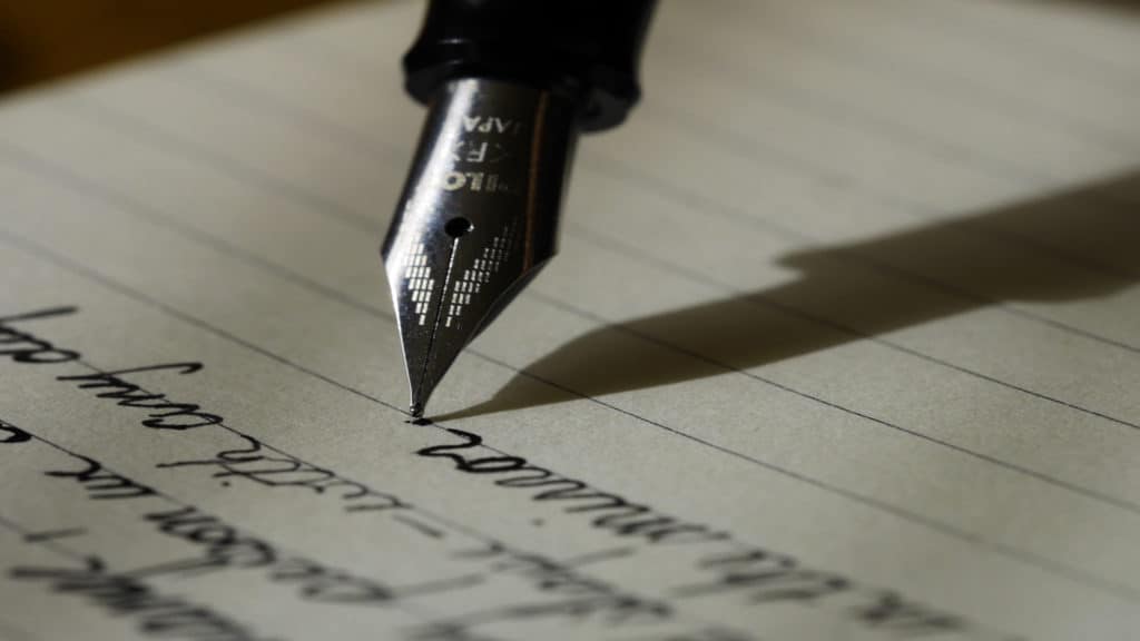 Close up of the tip of a fountain pen writing in cursive on a lined piece of paper