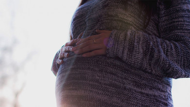 Close up of a pregnant woman's mid-section; she's resting her hands on her belly