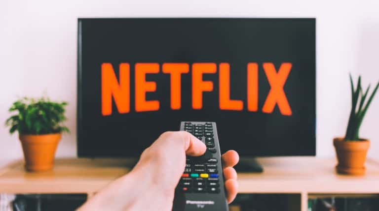 Close up of a hand pointing a remote at a TV displaying the Netflix channel