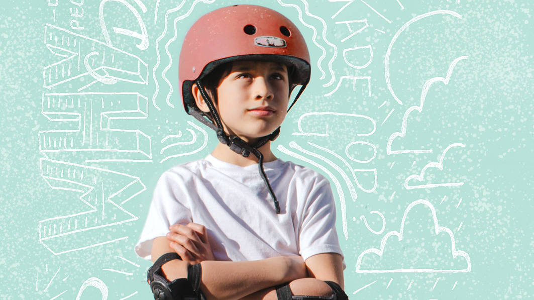 A young boy wearing bicycle helmet and elbow pads stands resolutely with arms folded