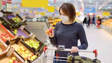 a woman wearing a surgical mask shops at a grocery store