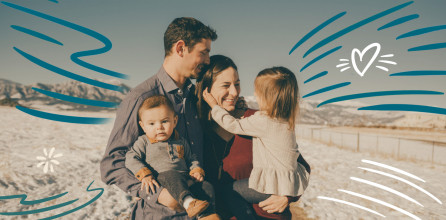 Happy young couple holding their two small children standing on a snowy field with mountains in the background