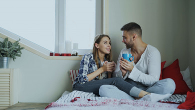 Young couple sitting on their bed drinking coffee and talking