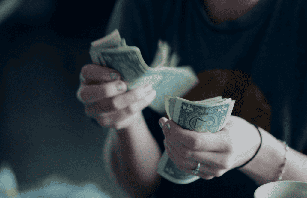 Close up of a woman's hands counting out a stack of one dollar bills