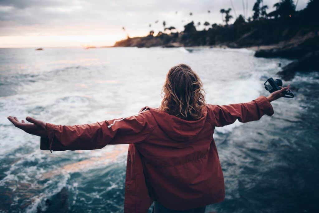 Woman standing by the ocean shore at sunset with her arms outstretched