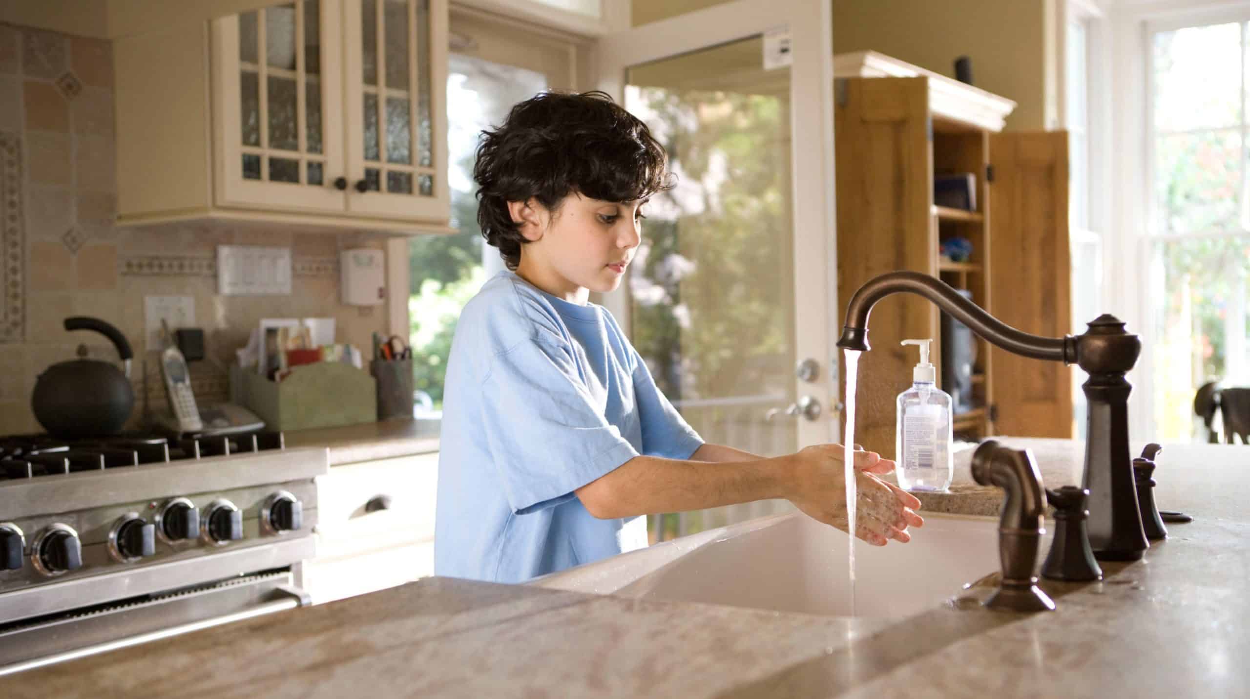 Child standing at a kitchen sink washing his hands
