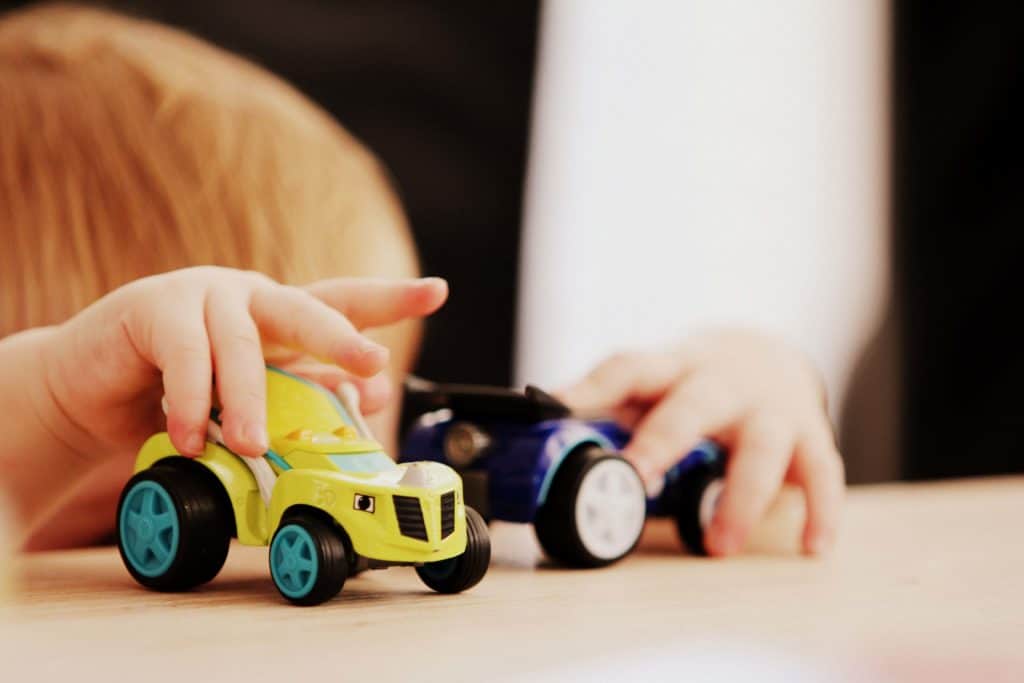 Close up of a young boy's hands driving two toy cars on a tabletop