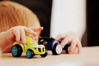Close up of a young boy's hands driving two toy cars on a tabletop
