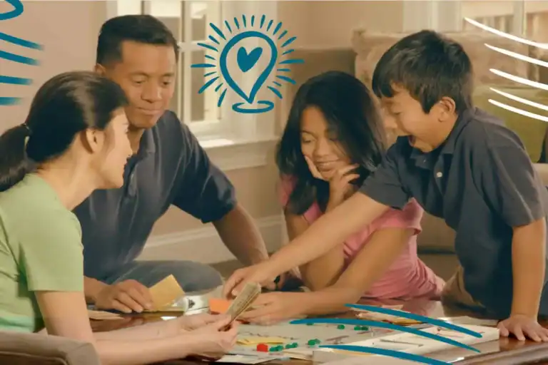 A family of four gathers around a board game at their living room table, playing games and activities to do with your kids as a way to bond and have fun together.