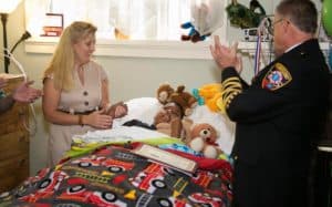 Ill or injured boy lying in his bed being presented with an award certificate by a uniformed official clapping his hands