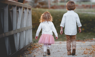 Shown from behind, a nicely-dressed young boy and girl walking over a bridge