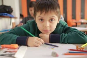 Close up of young boy at an art table, resting his head on his chin and looking into the camera