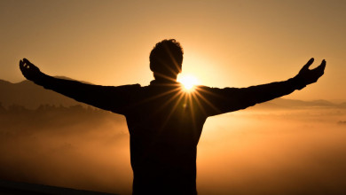 Silhouette of the back of a man with his arms raised up as he faces a sunrise