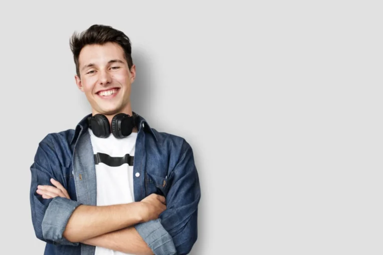 Teen boy with media headphones leaning against a wall and smiling at the camera