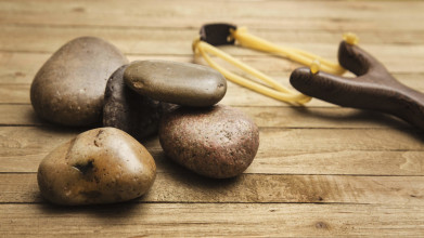 Close up of five smooth stones and a wooden slingshot lying on a wooden table