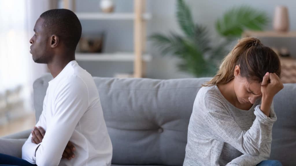 An upset young couple sitting on a couch with their backs toward one another