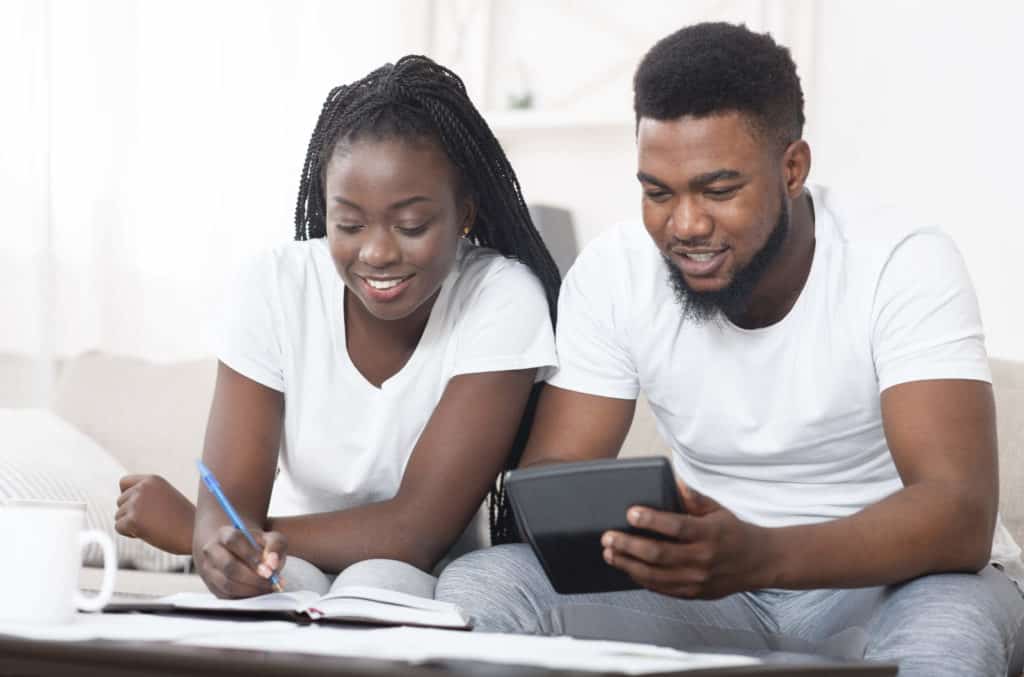 A happy-looking African-American couple sitting on their couch, working on their finances together