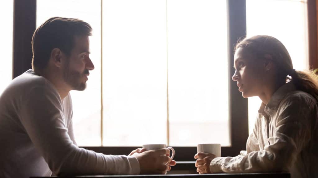 A young man and woman sit at a table and talk over a cup of coffee