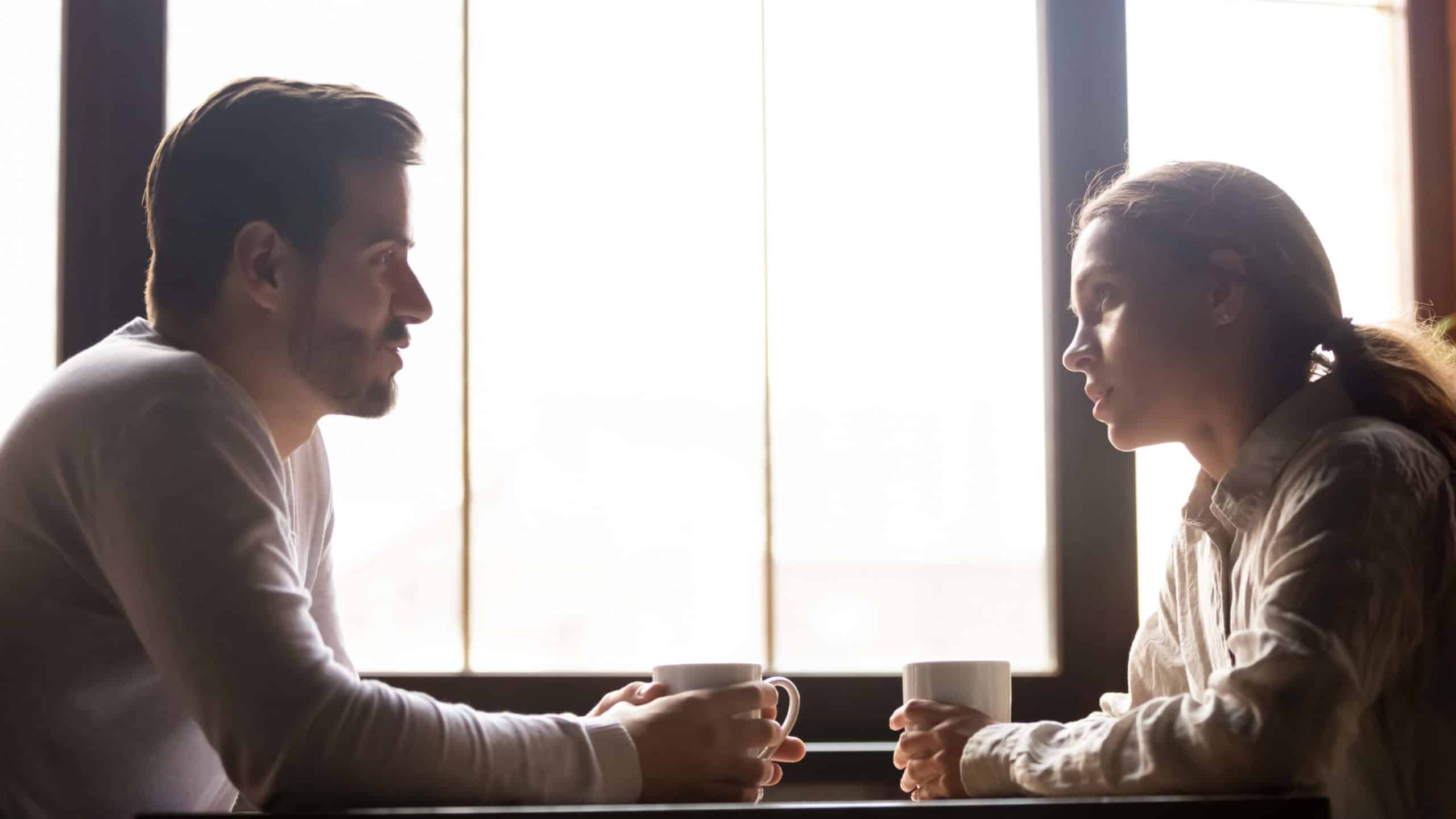 A young man and woman sit at a table and talk over a cup of coffee