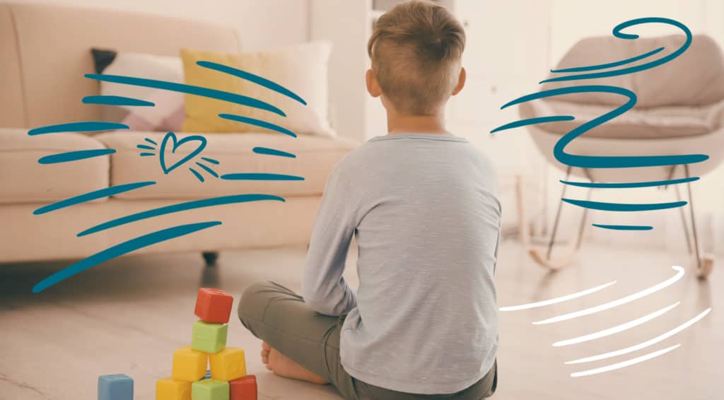 Shown from behind, a boy sitting cross-legged on the living room floor with a pile of toy blocks next to him