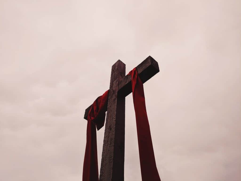 Upward-looking perspective of Christ’s cross with a red sash hanging on it and a cloudy sky as the background