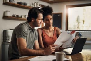 Young, interracial couple sitting at their kitchen table examining some documents