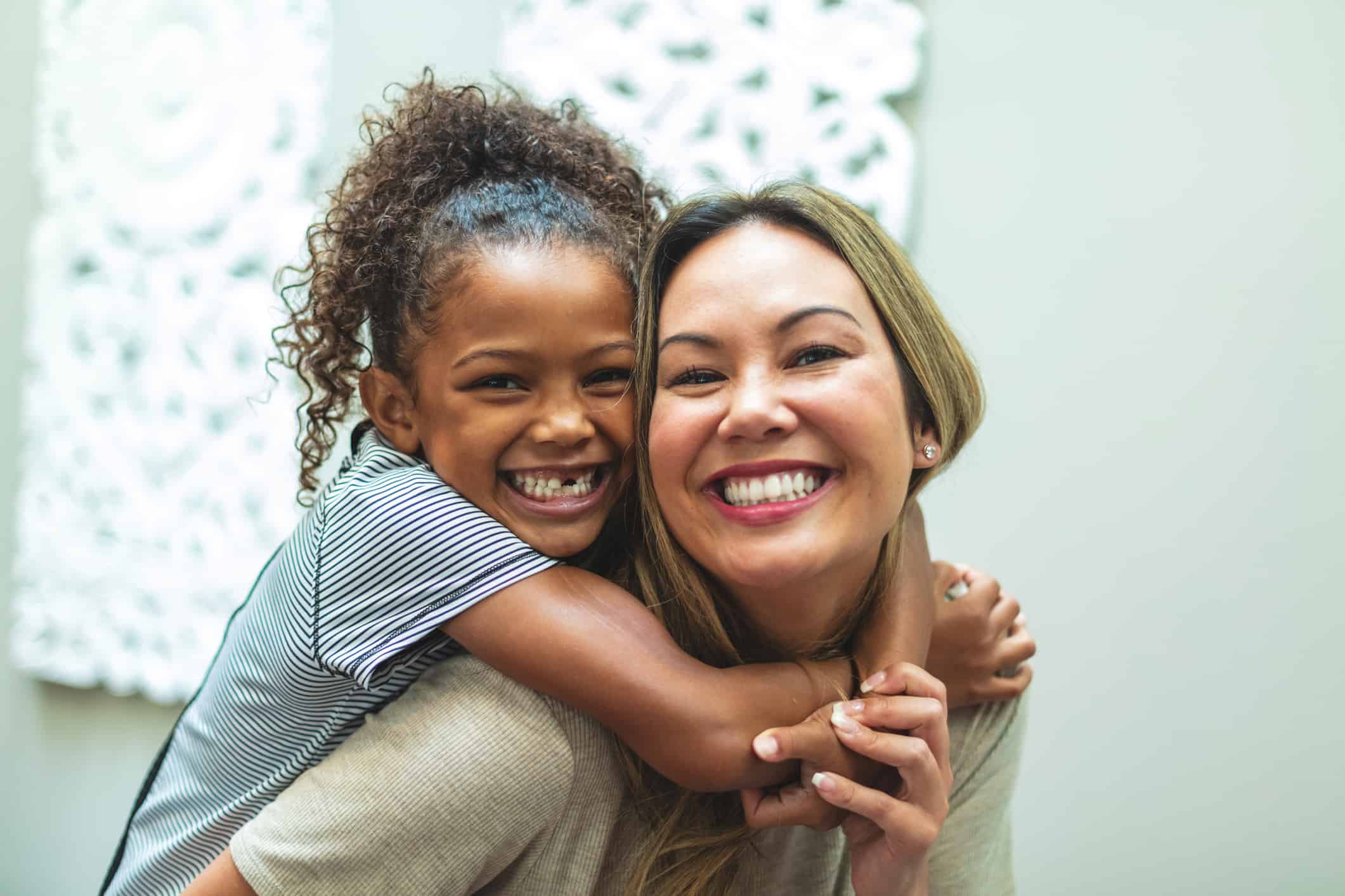 Woman giving a girl a piggyback ride; both are smiling happily