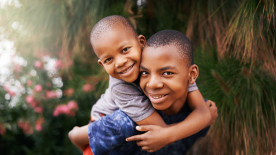 Black boy giving piggyback ride to his young brother; both are looking at the camera smiling