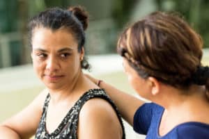 Close up of two women, one offering the other a compassionate arm around her shoulders